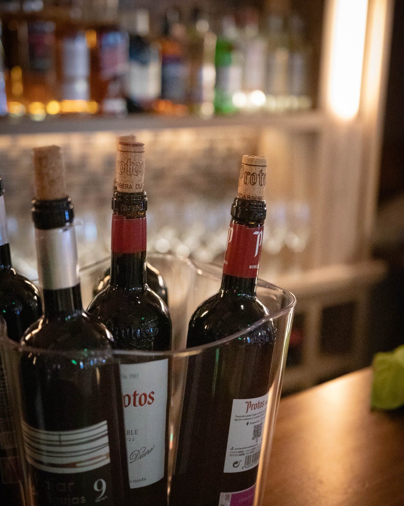 Botellas de vino en la cubitera de la barra, con las copas colgadas al fondo
