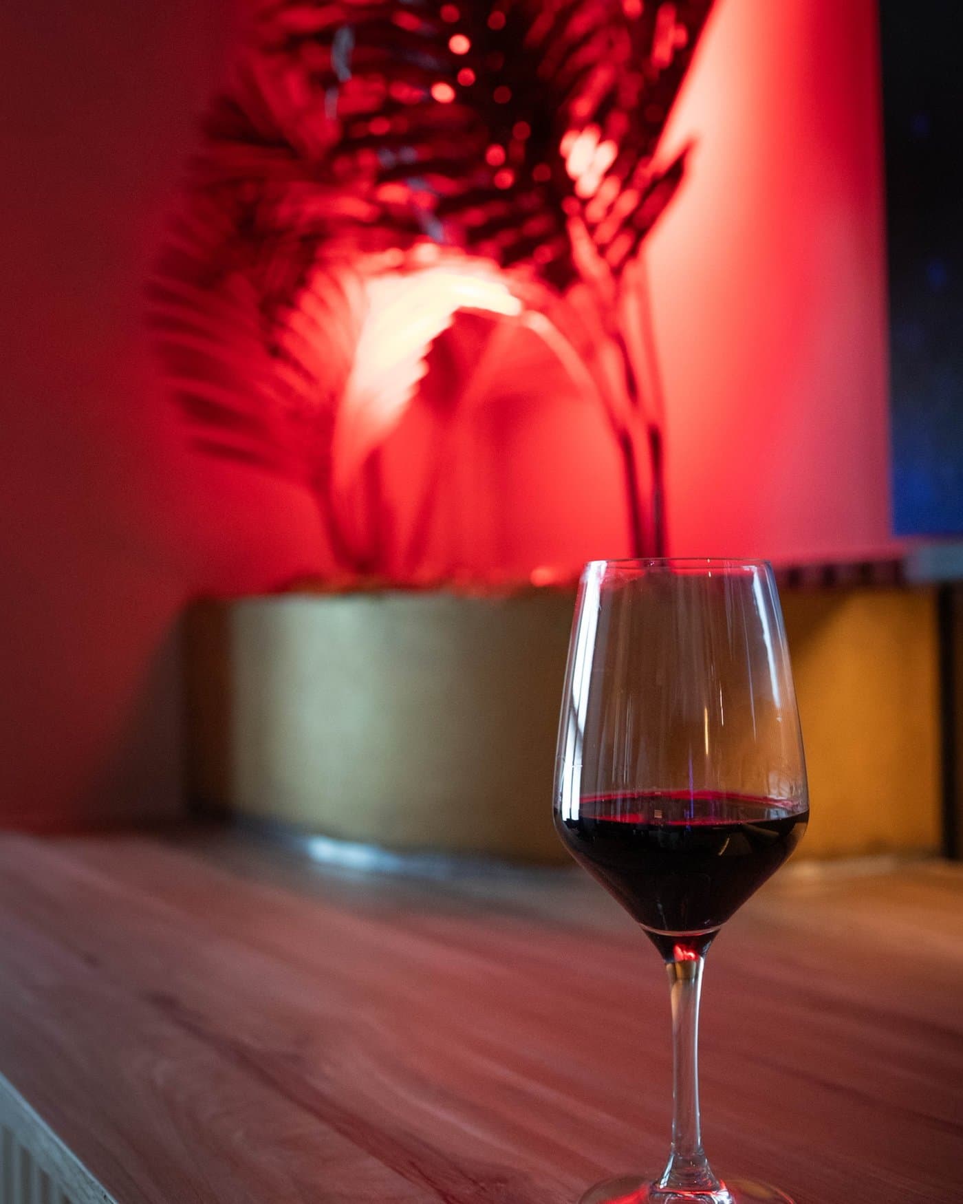 Copa de vino tinto sobre la barra, iluminada por la luz roja de la sala