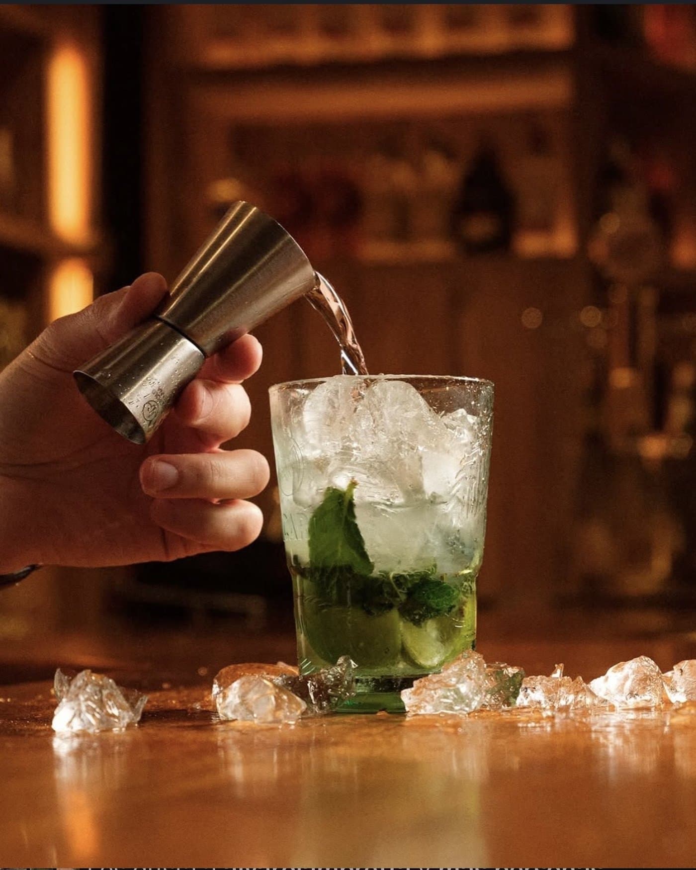 Camarero sirviendo ron con jigger sobre un mojito con hierbabuena y hielo picado