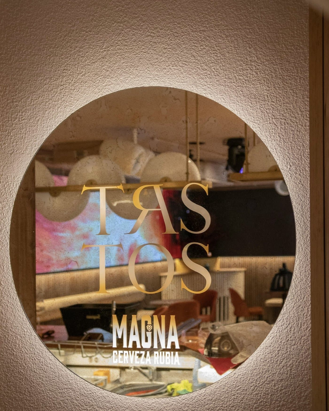 Ventana circular con el logotipo de Trastos rotulado en dorado sobre el cristal