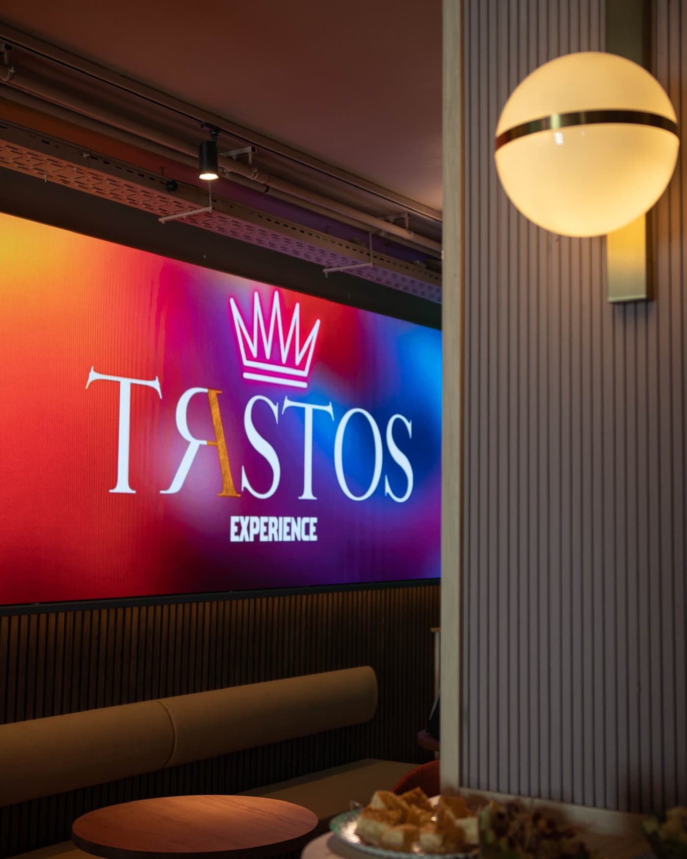 Pantalla LED de Trastos junto a un aplique esférico y los sofás de la zona de mesas
