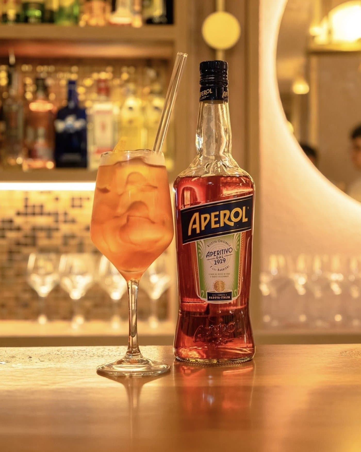 Spritz con hielo en copa de balón, junto a la botella de Aperol sobre la barra